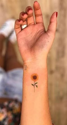 a woman's arm with a small sunflower tattoo on the left side of her wrist