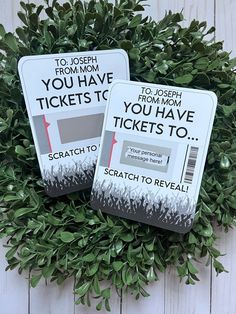 two tickets sitting on top of a green bush next to each other in front of a white wooden wall