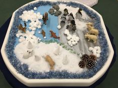 there are many different animals in the snow on this tray with rocks and pine cones