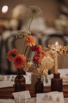 two vases with flowers are sitting on a table in front of candles and napkins