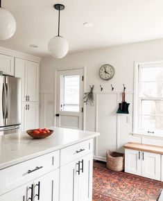 a bowl of fruit is on the counter in this white kitchen with an area rug