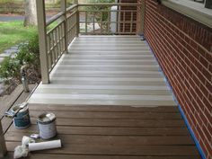 two cans of paint are sitting on the porch next to a brick wall and railing