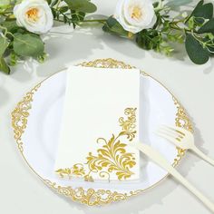 a white and gold plate topped with a napkin and fork next to flowers on top of a table