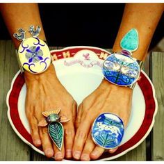 two hands with rings sitting on top of a white and red plate next to each other