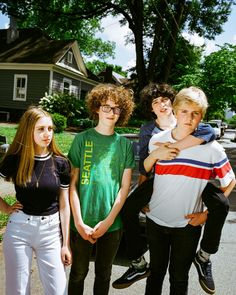 four young people standing next to each other in front of a house