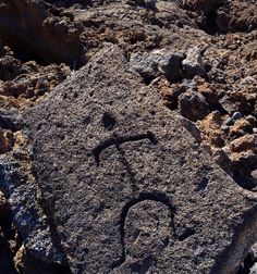 a rock with a face drawn on it in the middle of some dirt and rocks