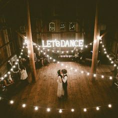 a bride and groom standing in the middle of a dance floor with lights strung around them