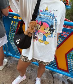 a person holding a small stuffed animal in front of a mickey mouse tee - shirt