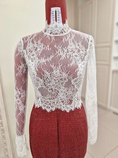 a mannequin wearing a white lace top and red pants in front of a mirror