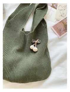 a green knitted bag sitting on top of a white bed next to a book