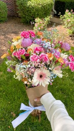 a bouquet of flowers is being held by a person's hand in the grass