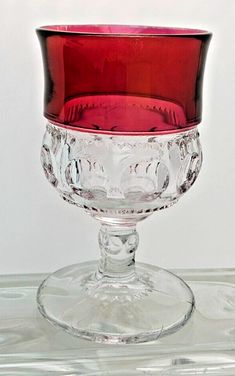 a red glass bowl sitting on top of a clear tableclothed surface with white wall in the background