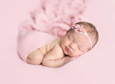 a newborn baby girl is sleeping on her side and wearing a pink headband with a flower in it's hair