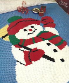 a crocheted blanket with a snowman on it and some candy in the background