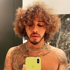 a man with curly hair looking at his cell phone in front of him is wearing a chain around his neck