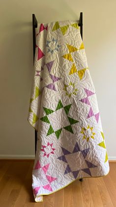 a white quilt with multicolored triangles on it hanging from a black iron frame