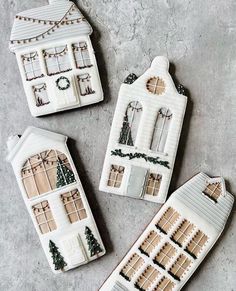 three gingerbread houses decorated with icing on top of a gray surface and surrounded by christmas decorations