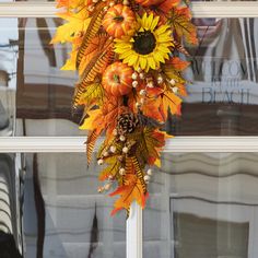 a wreath with sunflowers, pumpkins and other autumn decorations hanging on a window