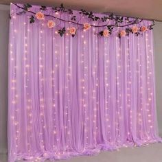 a purple backdrop with flowers and lights on the top is decorated in pink tulle