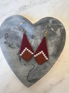 a pair of red and white beaded earrings sitting on top of a stone heart