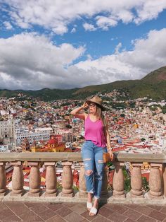 a woman standing on top of a balcony next to a tall building with a city in the background