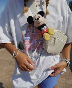 a woman holding a mickey mouse purse and a small stuffed animal in her pocket,