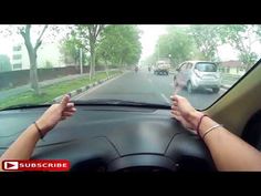 a woman driving a car down a street with her hands on the steering wheel