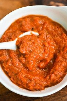 a white bowl filled with red sauce on top of a wooden table next to a spoon