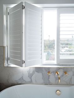 a white bath tub sitting next to a window with shutters on the windowsill