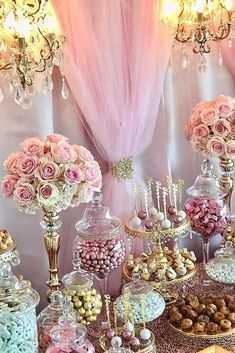 a table topped with lots of desserts and candy covered in pink flowers next to a chandelier