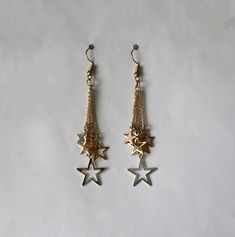 A fun pair of earrings consisting of many stars dangling on fine metal chains. There are solid stars and cutout stars, and there are three different metallic finishes.   The star charms are approximately 5/8 inches in diameter.  These earrings are approximately 3 inches in length.  Very cute! Thanks for visiting my shop. Metal Dangle Earrings With Star Charm, Star-shaped Metal Jewelry With Dangling Charms, Star-shaped Metal Earrings With Dangling Charms, Pleasant Grove, Earrings Star, Star Chain, Earrings Long, May 17, Chain Earrings