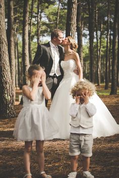 a bride and groom kissing in the woods with their two young children on their wedding day