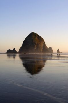 people are walking on the beach near an island in the ocean at sunset or dawn