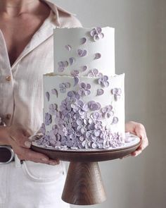 a woman holding a white cake with purple flowers on it