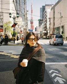 a woman is standing on the street holding a coffee cup and looking at the camera