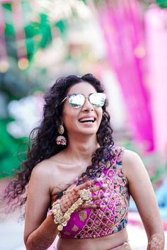 a woman in a pink and gold sari smiles while holding her hands out to the side