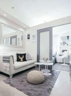 a living room with white furniture and gray rugs on the floor in front of a mirror