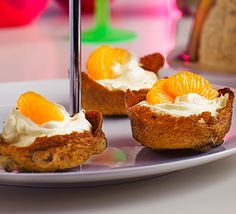 three small cupcakes on a plate with orange slices and whipped cream frosting