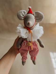 a hand holding a stuffed animal mouse wearing red and white striped pants with a red hat