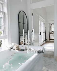 a bathtub with candles and flowers on it in front of a large mirror above the tub