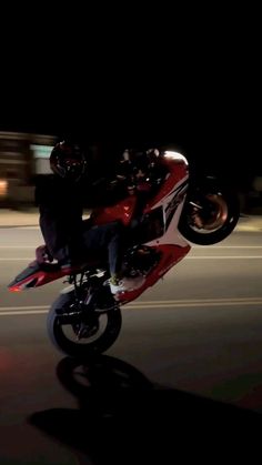 a man riding on the back of a red and white motorcycle in the street at night