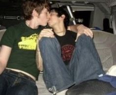 two young men sitting in the back of a car kissing each other with their legs crossed