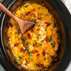 a crock pot filled with cheese, bacon and green onions next to a wooden spoon