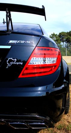 the back end of a black car with its trunk open and tail lights turned on