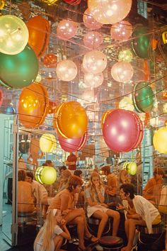 several women sitting on stools in front of a mirror with balloons hanging from the ceiling