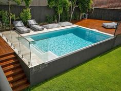 an above ground swimming pool surrounded by grass and wooden decking with lounge chairs around it