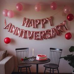 a happy anniversary balloon sign above a table with two chairs and a cake on it