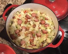 a pot filled with cabbage and sausages on top of a stove next to two red pots