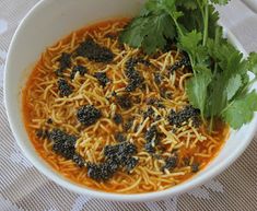 a white bowl filled with noodles and garnished with cilantro, parsley