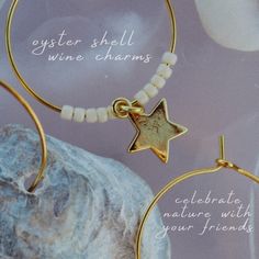 two gold hoop earrings with white beads and a star charm on them, sitting next to a rock